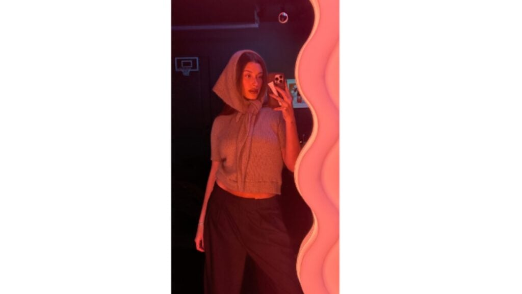Hailey Bieber posing in front of a mirror in crop top and pants.