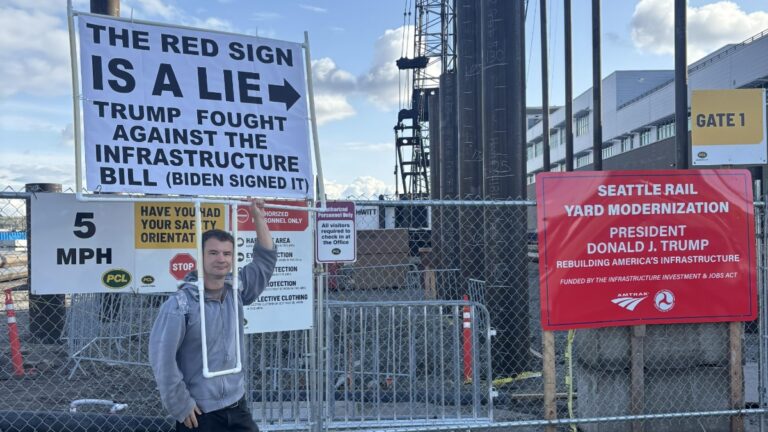 A Seattle man dons a large sign fact checking a nearby sign's claims about Trump